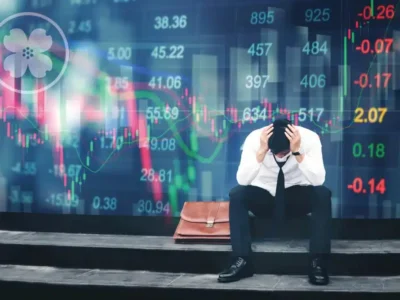 Man Sitting On The Ground Looking Down With His Hands Over His Head Stressed About The Stock Market.