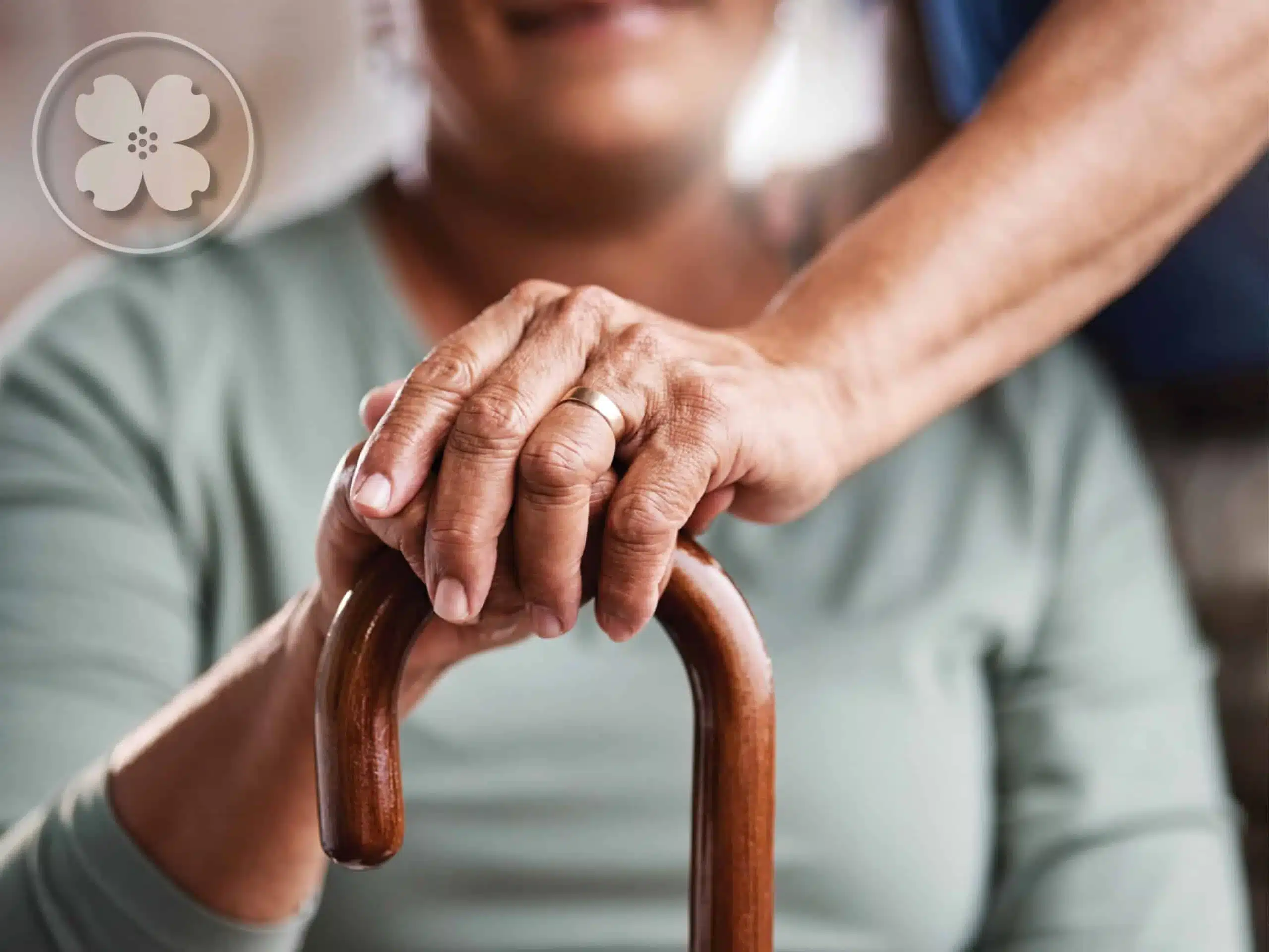 Elderly couple with hands stacking on top of each other on a walking cane.